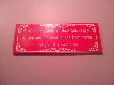 A sign in a Greensboro, NC restaurant that reads, "Here in the South, we don't hide crazy... We parade it around on the front porch and give it a sweet tea."